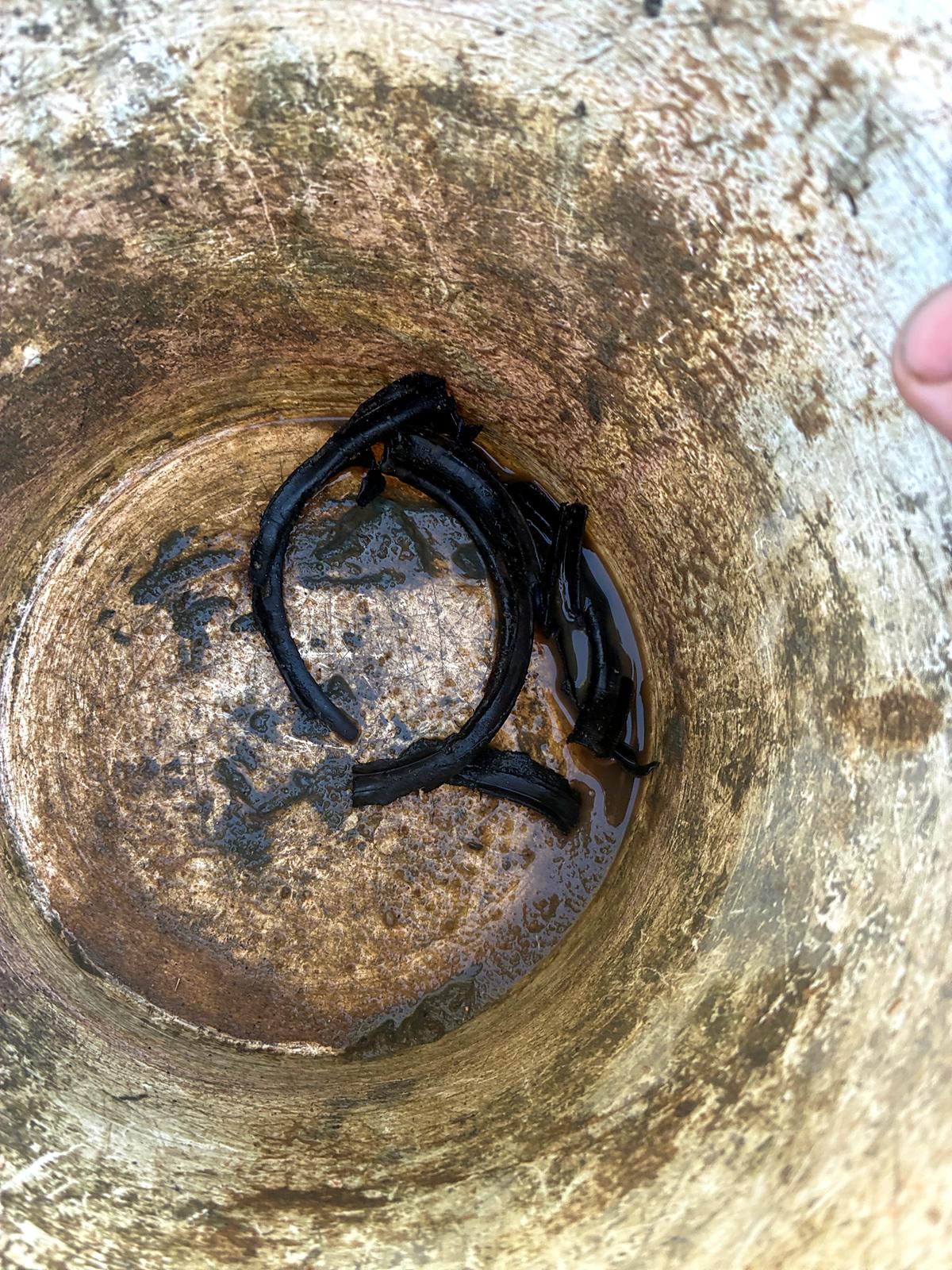 Cut sections of black agg pipe sitting in water at the bottom of a drainage pit after being trimmed out of the line